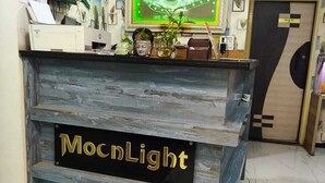 A reception desk with a sign reading 'MocnlLight,' a wall-mounted television, and a fan above the desk. - Hotel Moon Light Indore (Indore)