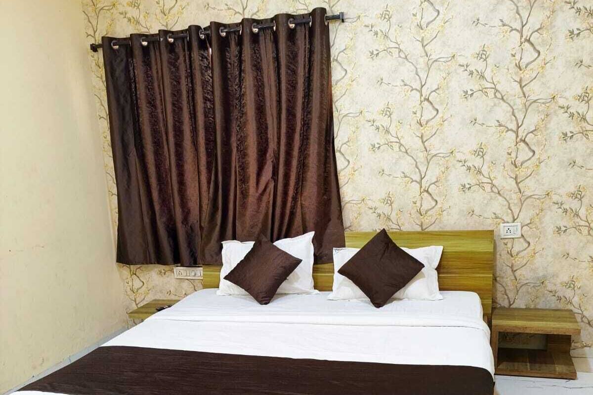 Una cama individual con estructura de madera, ropa de cama blanca y dos almohadas marrón oscuro. Junto a la cama hay una mesita de noche de madera.