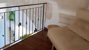 A room with a wooden floor, a beige sofa, a balcony with a metal railing, and a green vase on the windowsill. - At Vico 12 (Monopoli)