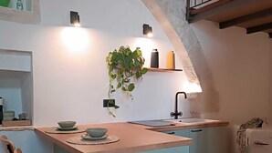 A compact kitchen with a central island, a sink, and a small refrigerator. There are two bar stools and a potted plant on the island. - At Vico 12 (Monopoli)