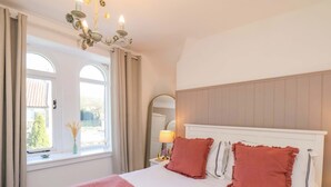 A bedroom with a large bed, a chandelier, a window with curtains, and a view of the outside. - 1 Rosedale Abbey (Pickering)