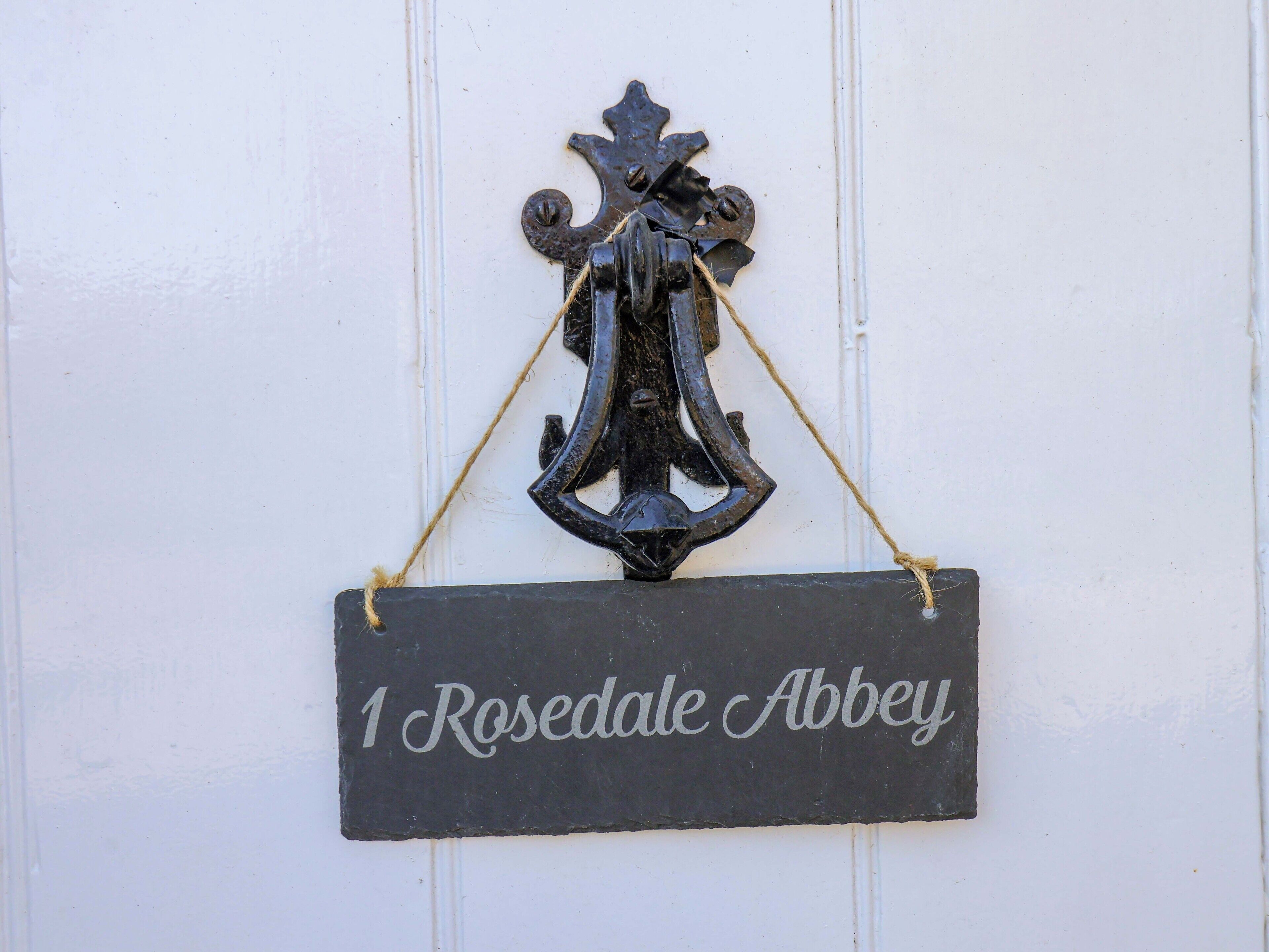 Une plaque noire avec une inscription blanche en lettres cursives indiquant « 1 Rosedale Abbey », fixée à un mur blanc.