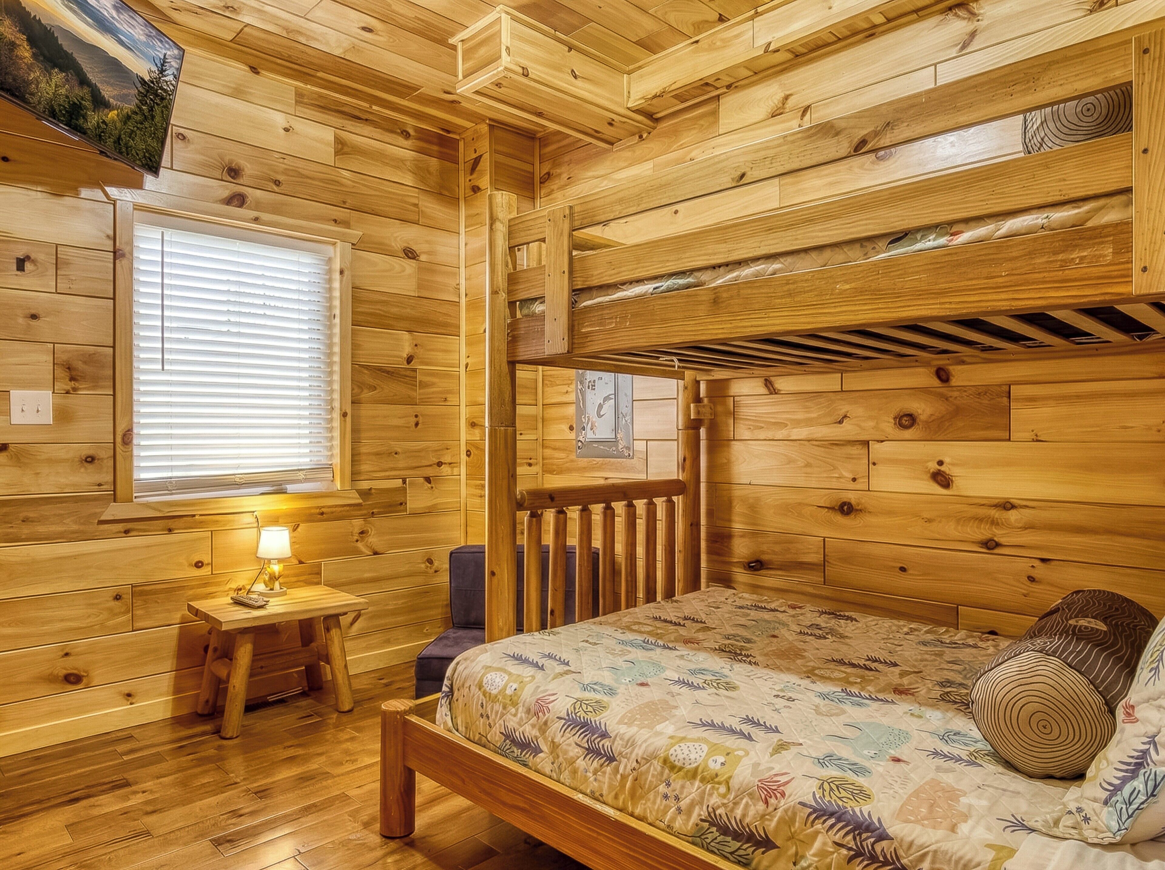 A wooden cabin room with a bunk bed, a small table with a lamp, and a window with blinds.