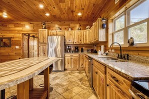 A kitchen with wooden cabinets, a stainless steel refrigerator, a granite countertop, and a window with a view. - Beartastic Mountain View Lodge, Game Room, Hot Tub! (Gatlinburg)