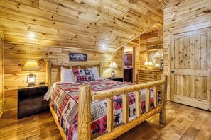 A wooden cabin-style room with a bed, nightstands, a dresser, and a door. - Beartastic Mountain View Lodge, Game Room, Hot Tub! (Gatlinburg)