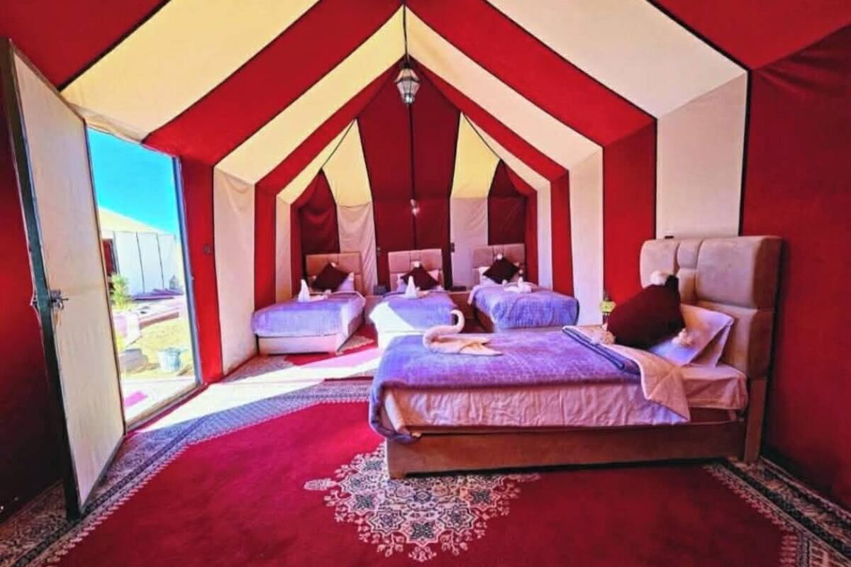 Un hébergement sous tente doté de deux lits, d’une décoration aux couleurs rouge et blanche, et offrant une vue sur l’extérieur.