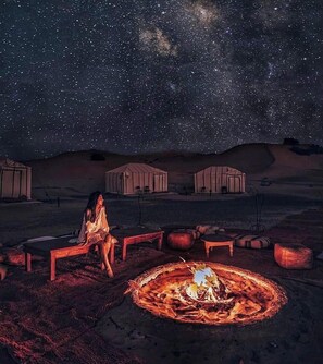 A starry night sky with a campfire and yurts in a desert setting.
