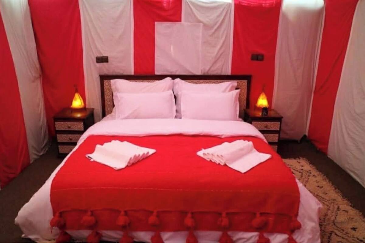 Un lit avec une couvre-lit rouge et des oreillers blancs, deux lampes de chevet et un drapé décoratif rouge et blanc.