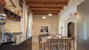 A rustic kitchen with stone walls, wooden beams, and a dining area with wooden chairs and a table. - Rhadamanthus By Forest Villas (Rethymno)