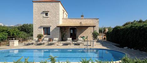 A stone building with a swimming pool, outdoor seating, and a view of the surrounding landscape.