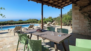 A covered outdoor area with a pool, lounge chairs, and a table with fruit and water glasses. - Rhadamanthus By Forest Villas (Rethymno)