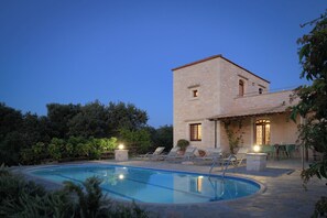 Un edificio de piedra con piscina, sillones de descanso y un patio.