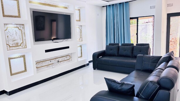 Een moderne woonkamer met een grote flatscreen-tv, zwarte leren banken en een witte entertainmentkast met gouden accenten.