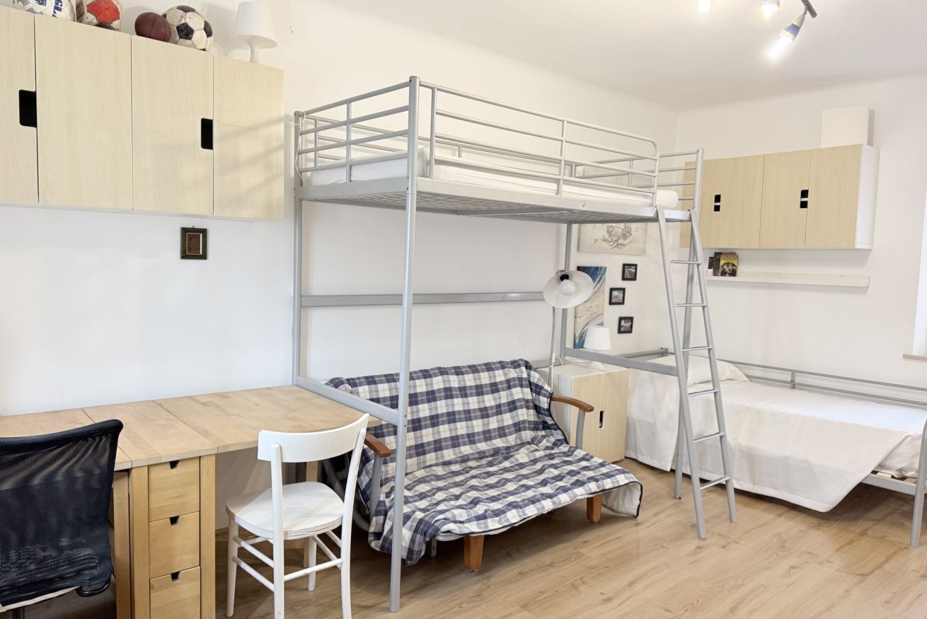A bunk bed room with a desk, chair, and a checkered blanket.