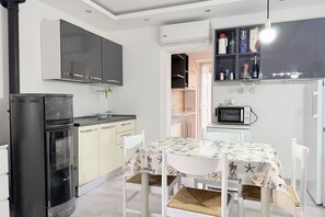 Una cocina compacta con un refrigerador negro, armarios blancos, un microondas y una mesa de comedor con mantel decorado con motivos náuticos.
