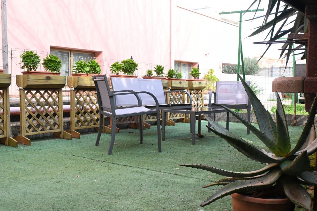 Un patio con mobiliario exterior, plantas en macetas y césped artificial verde.