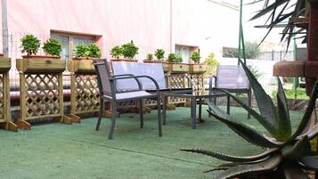Un patio con mobiliario exterior, plantas en macetas y césped artificial verde.