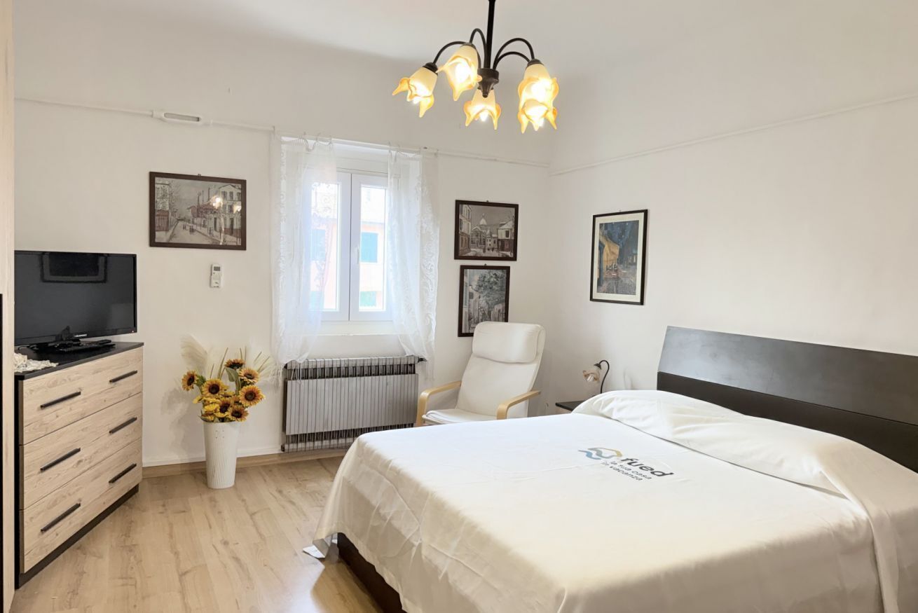 Une chambre d’hôtel avec un lit, une télévision, une chaise, un bureau et une fenêtre avec des rideaux.
