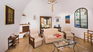 Una sala de estar con chimenea, dos sillones, un sofá, una mesa de centro y una araña.