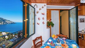 Un balcón con techo de madera, una mesa de comedor dispuesta con comida y vista al mar.