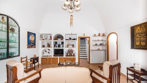 Un salón espacioso con un techo alto en arco, muebles de madera, un televisor y una estantería llena de objetos decorativos.