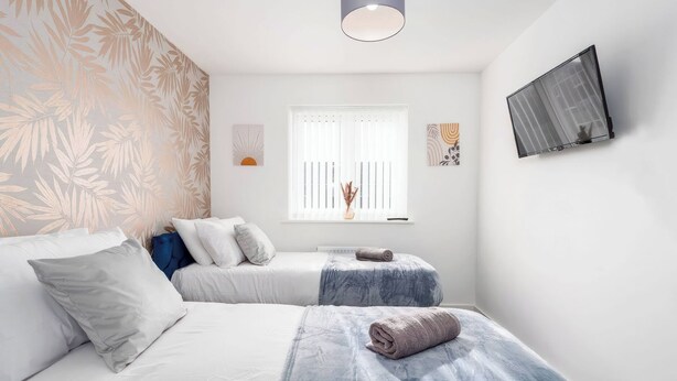 A bedroom with two beds, a window with blinds, a wall-mounted TV, and a ceiling light. - 59 Eagle Drive (Grimsby)