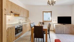 Een moderne keuken met houten kasten, een eettafel, stoelen, een televisie en een kroonluchter.