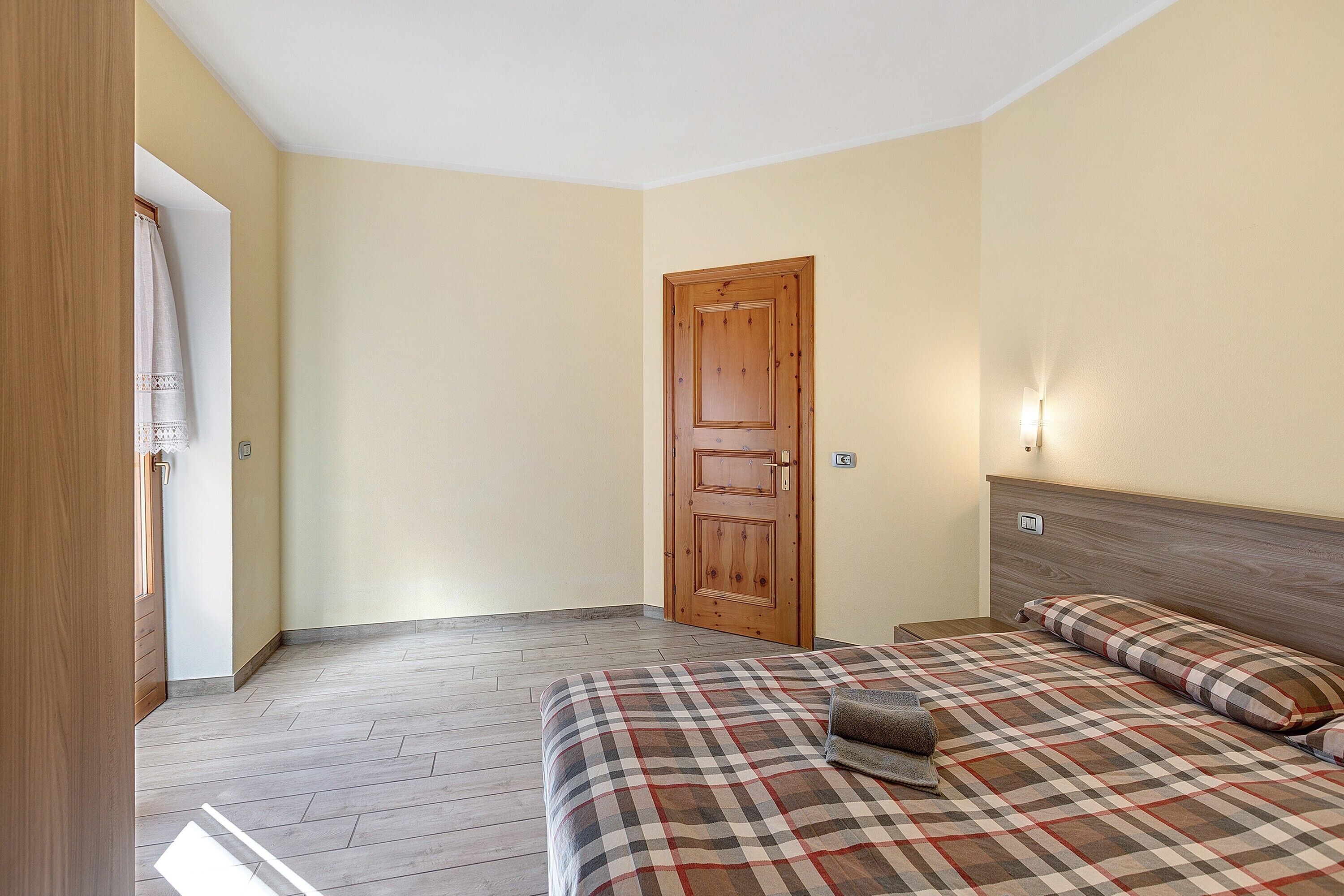 A bedroom with a wooden door, a bed with a plaid bedspread, and a nightstand.
