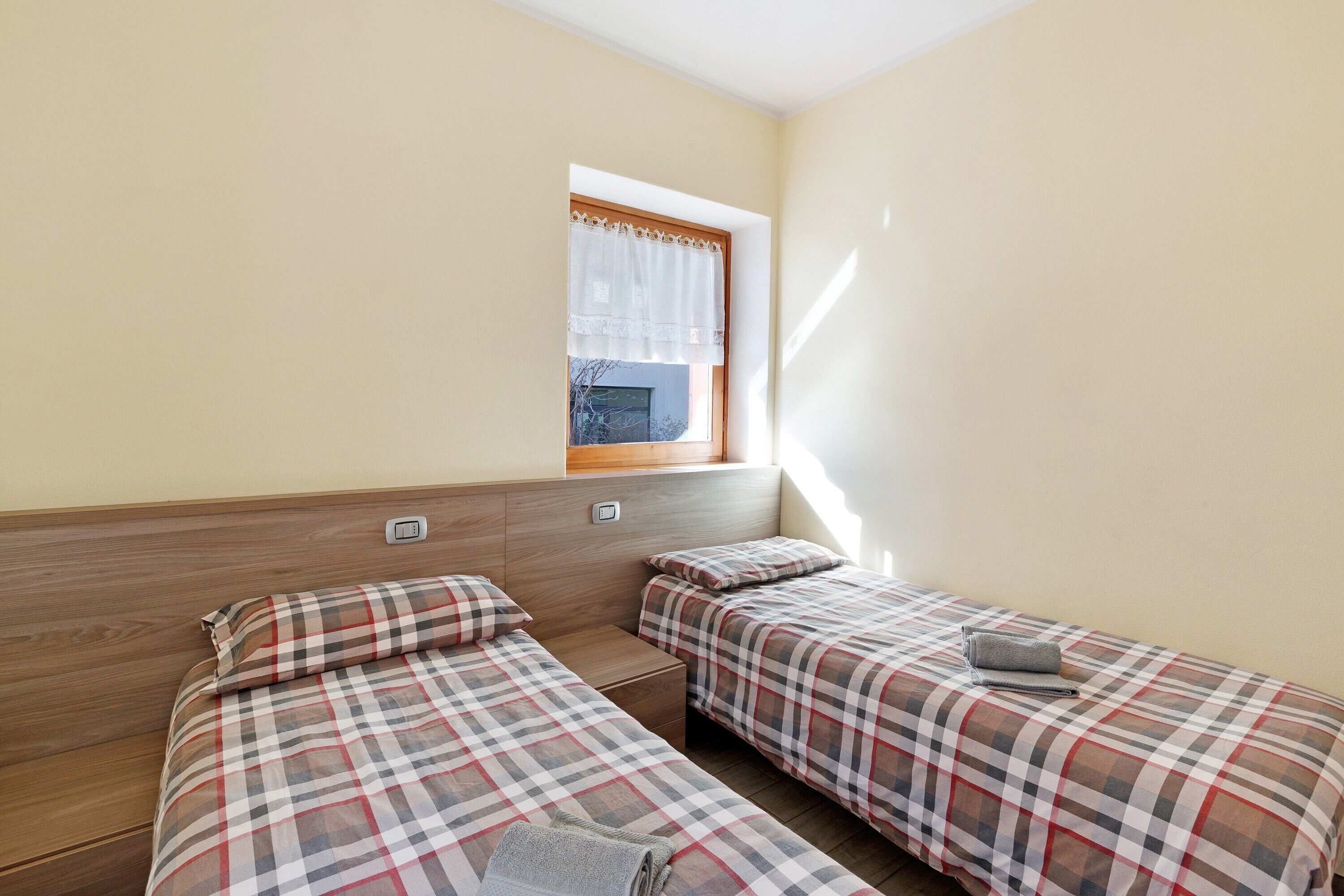 A room with two beds, a window with a curtain, and a wooden headboard.