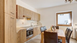 Een moderne keuken met houten kastjes, een inbouwoven en een eethoek met een tafel en stoelen.