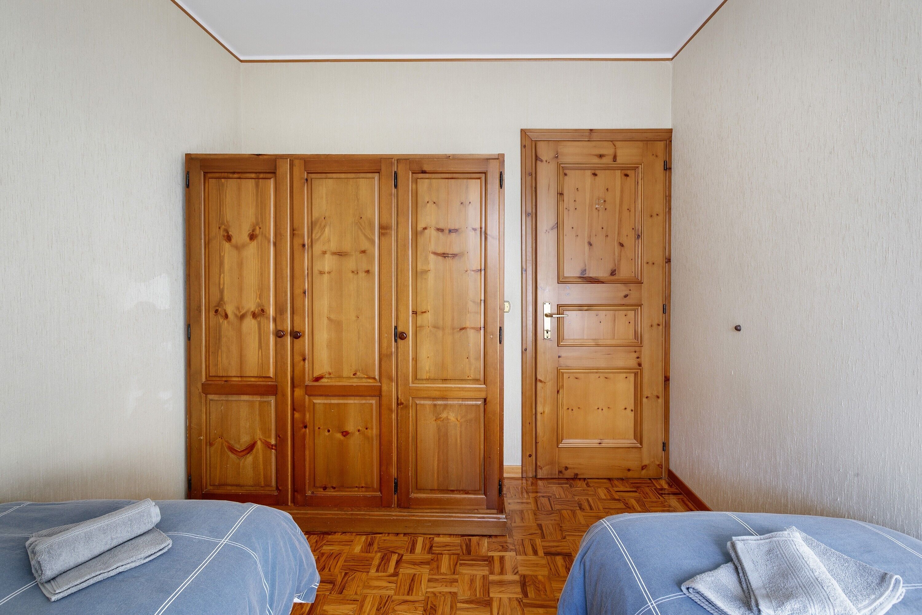 Une chambre avec deux lits, des armoires en bois et un parquet à motifs en chevrons.