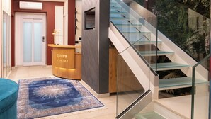 Een moderne lobby met een receptiebalie, een trap met glazen balustrades en een decoratieve wand.