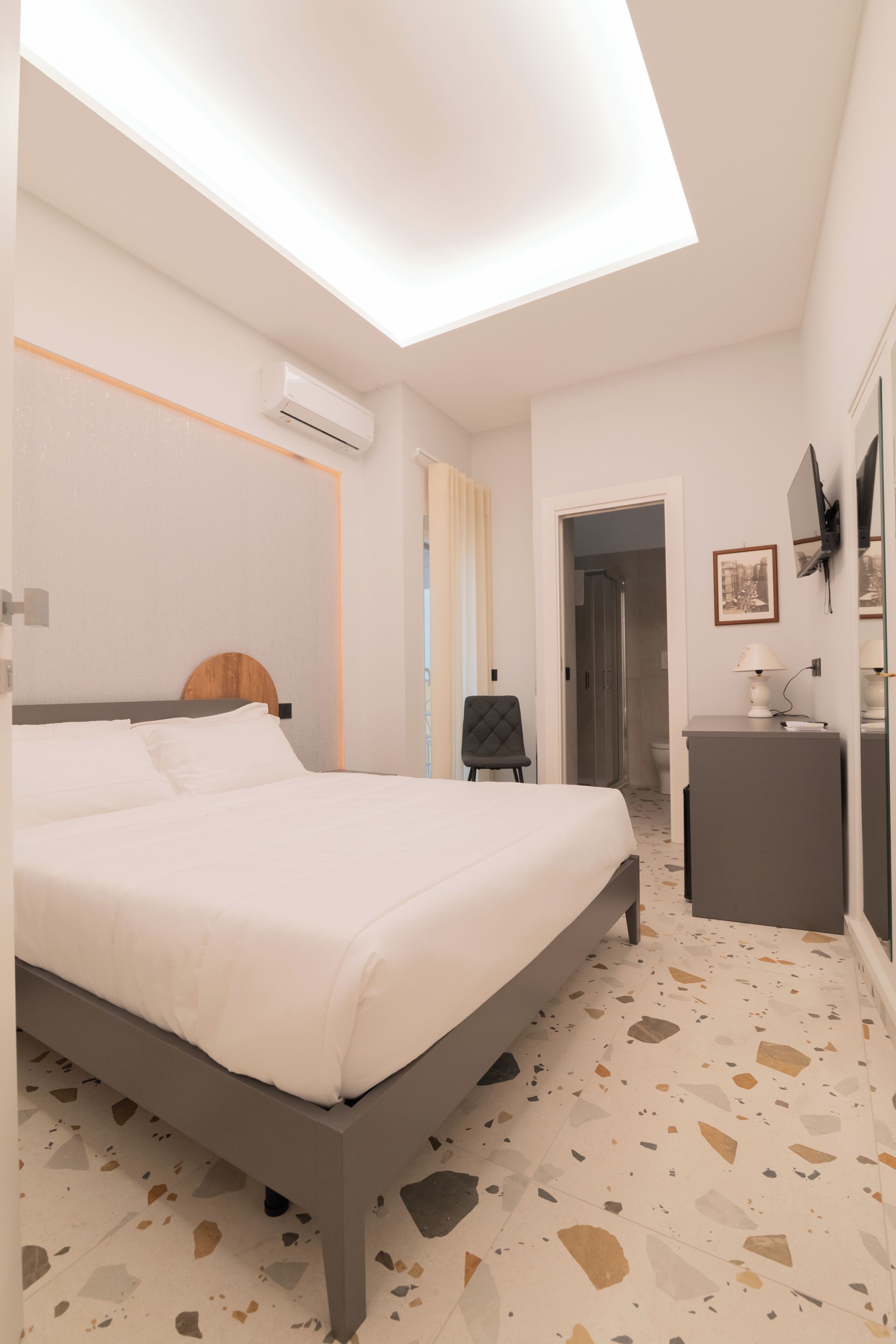 A bedroom with a bed, a desk, an air conditioner, and a door leading to a bathroom.