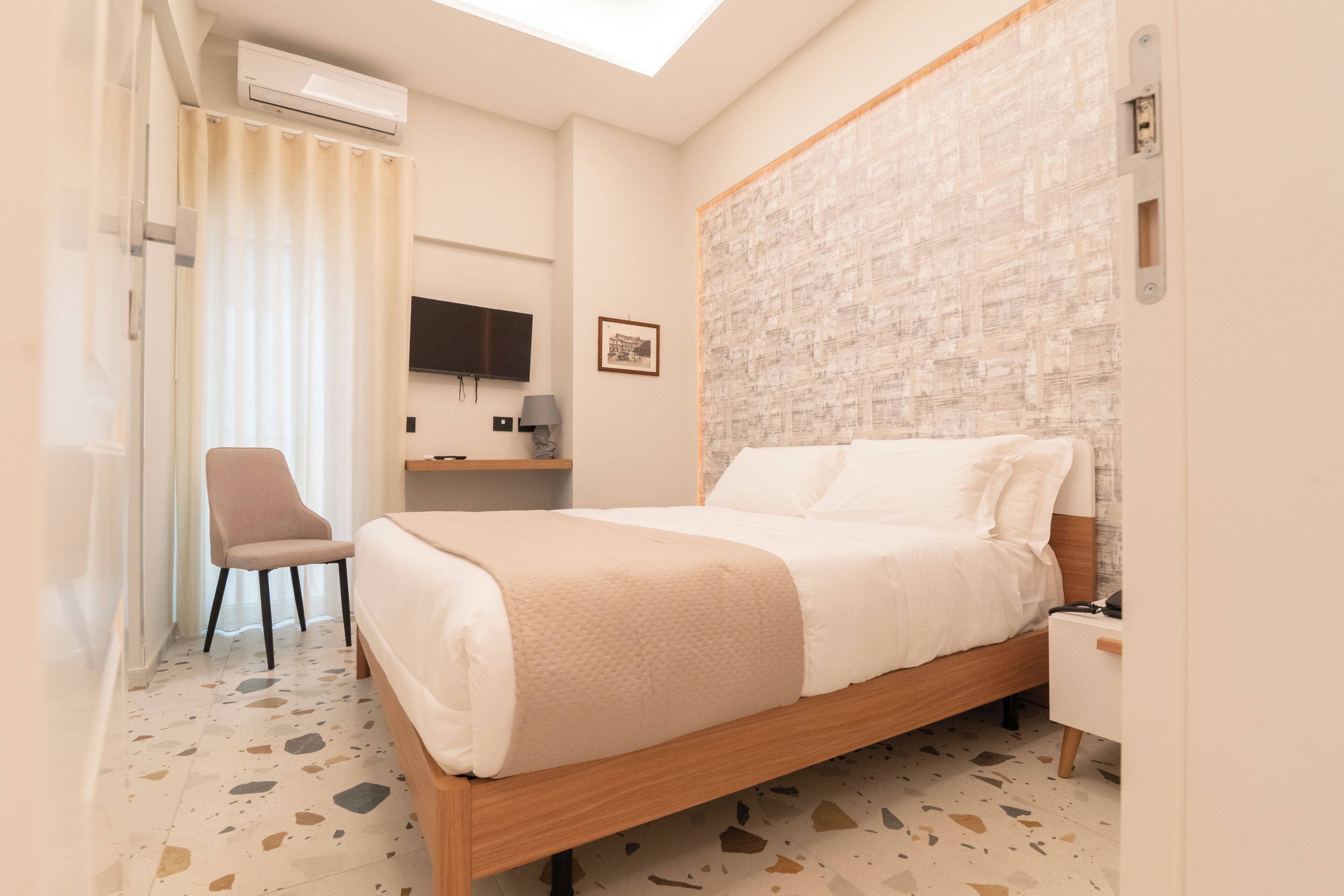 Une chambre d’hôtel équipée d’un lit, d’une chaise, d’un bureau avec un ordinateur et d’un téléviseur fixé au mur.