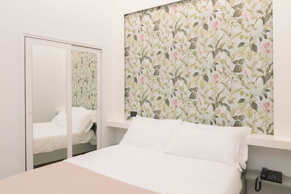 Une chambre à coucher avec un lit, une table de chevet avec un téléphone, un miroir et un papier peint à motifs floraux.