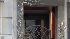 Een ijzeren hekwerk met decoratieve details, een metalen deur met ruitmotief en een naambordje aan de muur.