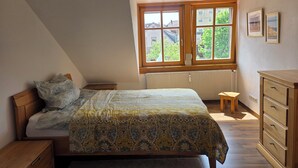 A bedroom with a bed, a window, a radiator, a wooden dresser, and a small stool. - "Saskia" Vacation Rental with a Beautiful View of the Old Town and a Rooftop Terrace! (Hammelburg)