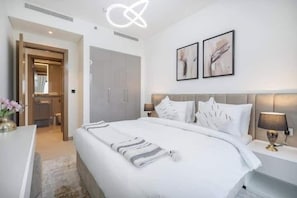 A modern hotel room with a large bed, a bedside table with a lamp, and a wardrobe. - Vogue | Sobha Hartland close to Downtown Dubai Mall | Burj Khalifa (Dubai)