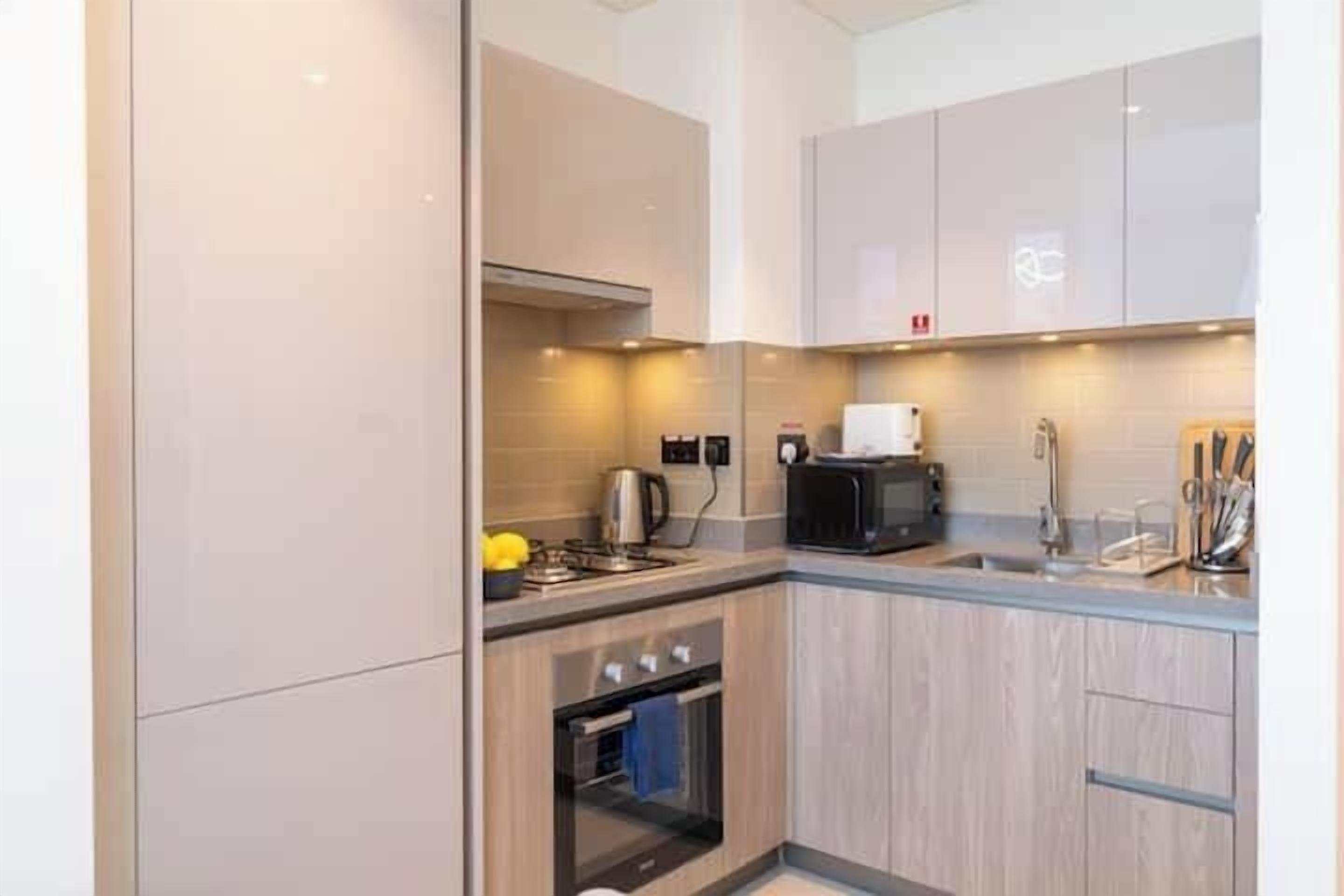 A modern kitchen with light wood cabinetry, a built-in oven, a coffee machine, and a kettle.