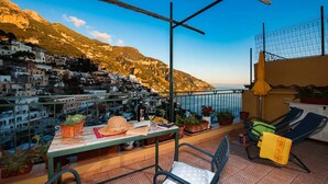 A terrace with a table, chairs, potted plants, and a view of a hillside town. - Rifugio con Terrazza Panoramica a Positano (Positano)