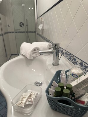 A bathroom sink with a towel, toiletries, and a shower area in the background. - Rifugio con Terrazza Panoramica a Positano (Positano)