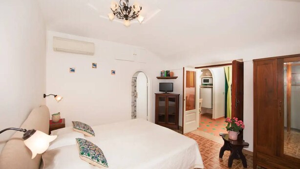 A bedroom with a bed, bedside lamp, TV, and a small cabinet. - Rifugio con Terrazza Panoramica a Positano (Positano)