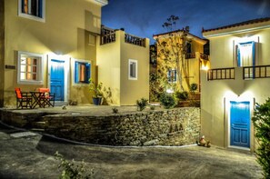 Un patio con un muro de piedra, una mesa pequeña con sillas y un edificio con puertas y ventanas azules.
