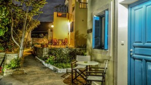 A courtyard with a table and chairs, a blue door, and a building with a balcony. - Mainades Studio - Evrypyli Serene Escape in Andros (Andros)