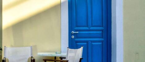 Une porte bleue avec un trou de serrure et une poignée, une petite table ronde et deux chaises blanches avec des sièges en tissu.