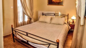 A neatly made bed with a metal frame, a bedside table with a lamp, and a painting on the wall. - Mainades Maisonette - Andros Seaview Escape (Andros)
