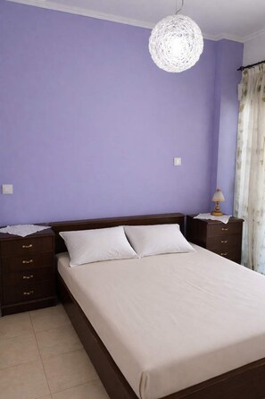 A bedroom with a large bed, two nightstands, a lamp, and a decorative ceiling light. - Absolute Beachfront Bliss in Perigiali Korinthia (Corinth)