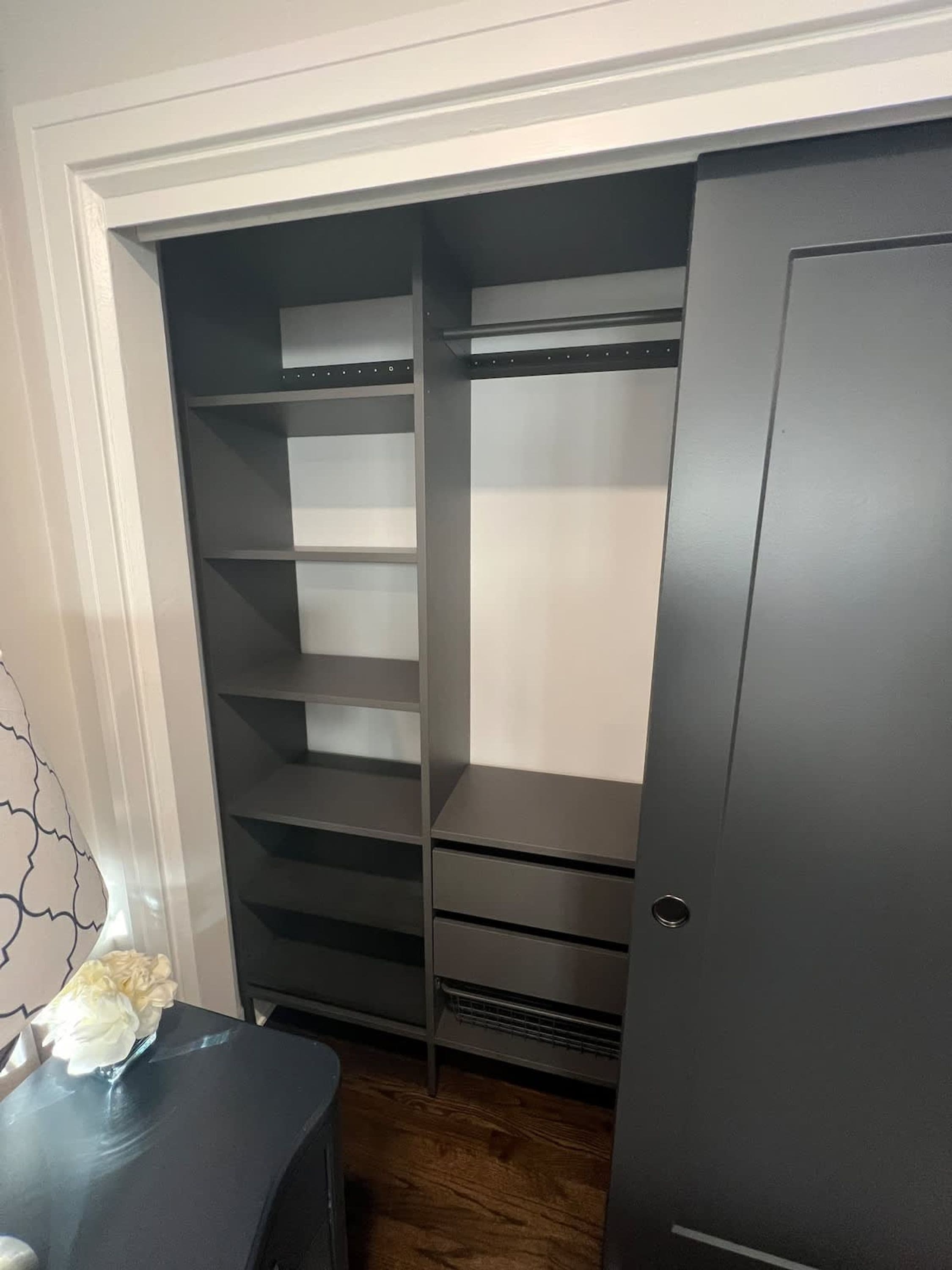 Ein begehbarer Kleiderschrank mit mehreren Regalen und Schubladen, einer Tür und einem kleinen Tisch mit einer Vase.