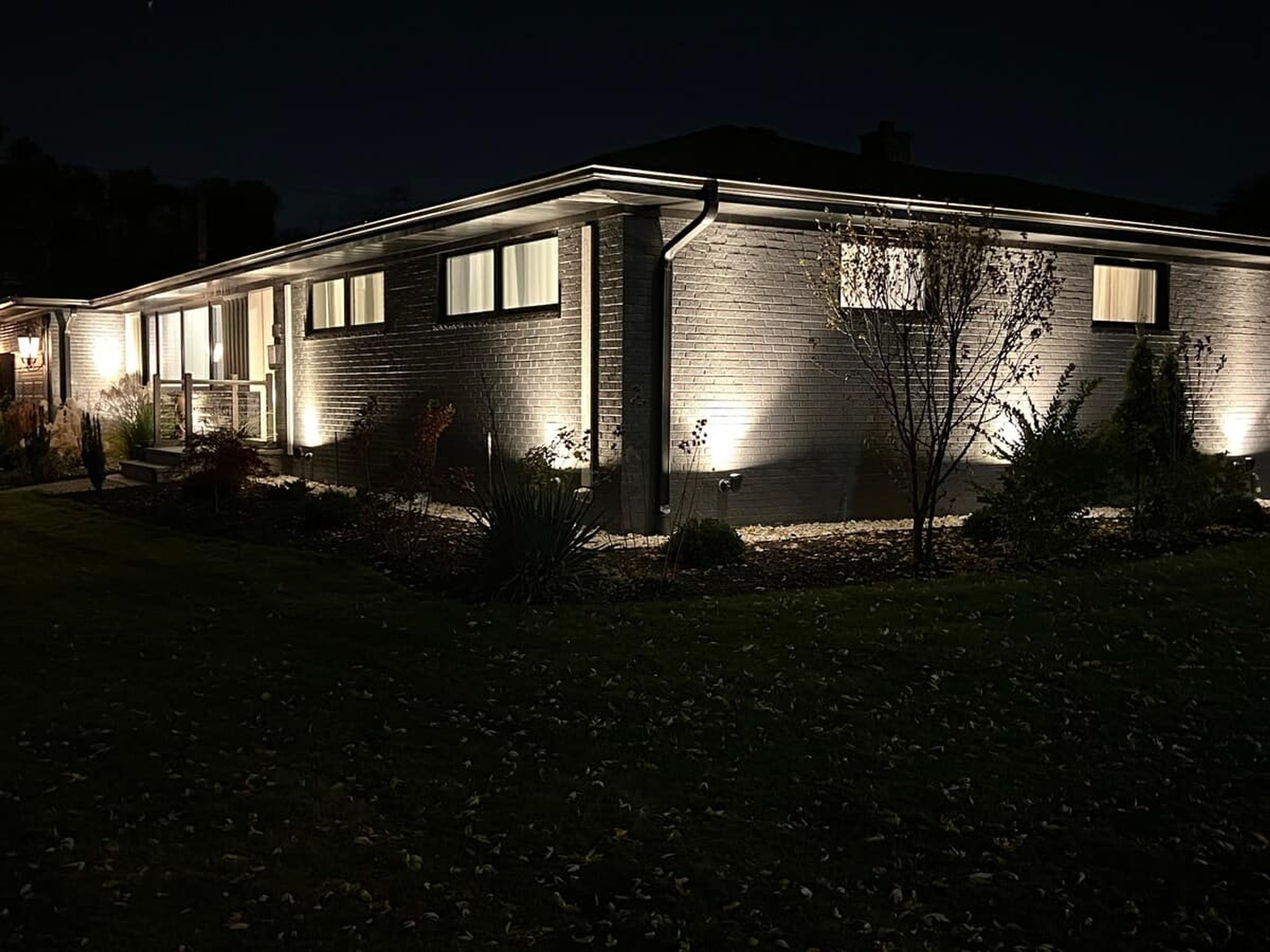 A two-story house with a brick exterior, illuminated windows, and a well-maintained front yard.