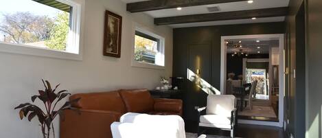 Una sala de estar moderna con un sofá de cuero marrón, un sillón blanco y una planta en maceta. Se ve una escalera que lleva a otra habitación.
